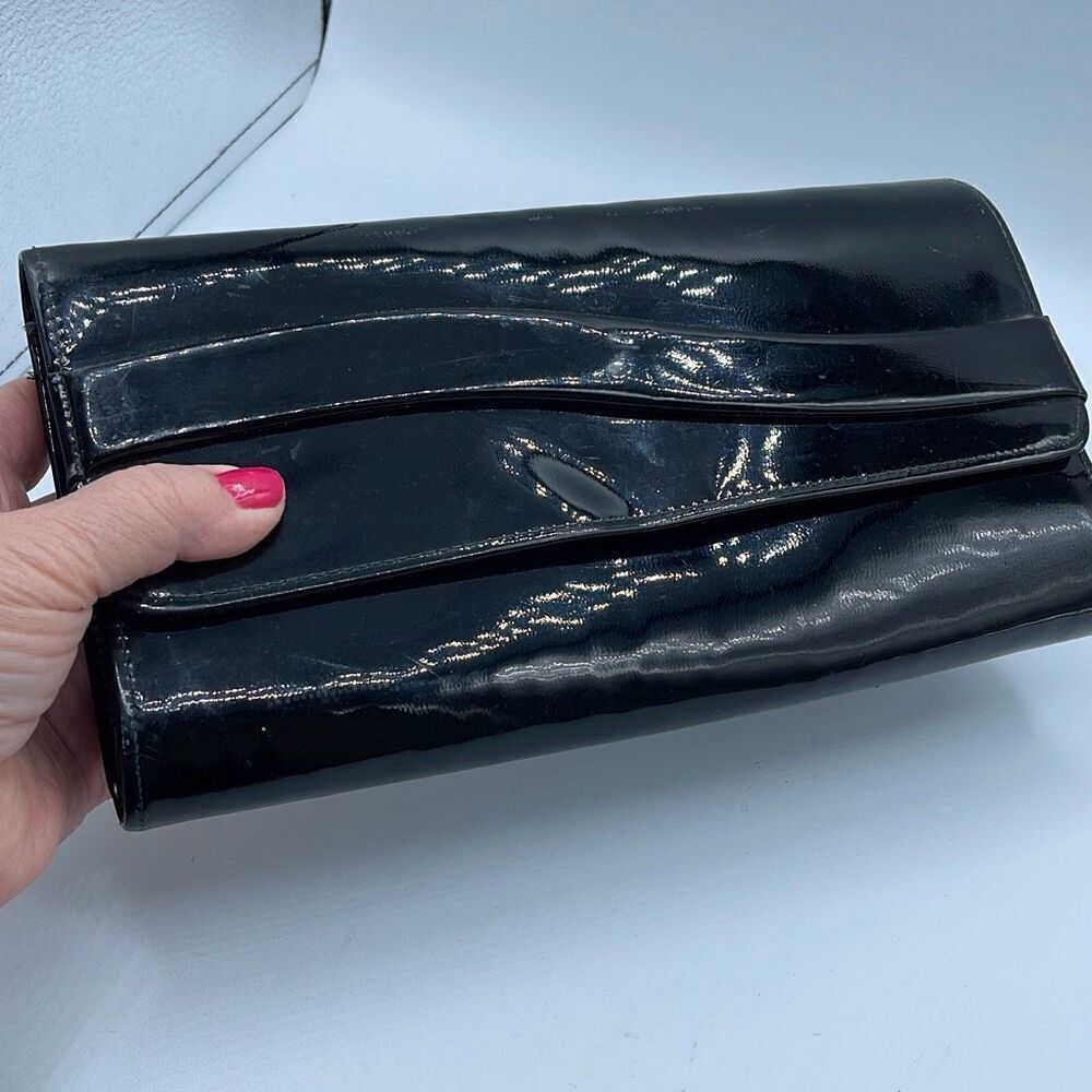 Black faux patent leather clutch with wave design on front.